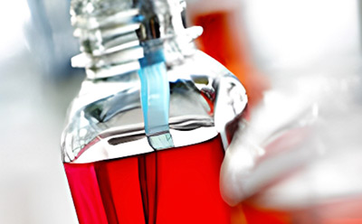 Close-up view of a laboratory technician’s hand fastening a blue strap around the metallic lid of a red media bottle, ensuring a secure seal for media storage in a laboratory setting. Media Preparation