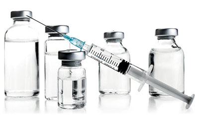 Matières premières pour la biotransformation et la formulation Une seringue médicale avec une aiguille, partiellement remplie de liquide, est placée en diagonale devant cinq flacons de différentes tailles avec des bouchons métalliques sur un fond blanc.