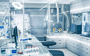 Certified Reference Materials Lab with white cupboards and chemistry lab equipment used for quantitative analysis is shown without any people working. Fume hood, glass vials and beakers are visible.