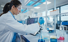 Réactifs Une laborantine portant des lunettes de protection et des gants en nitrile prépare une solution de réactifs dans des béchers contenant des liquides bleus et roses.