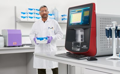 前臨床開発 顕微鏡、CellASIC<sup>®</sup> ONIX2ライブセルイメージングシステム、コンピューターモニターが置いてあるベンチの前に座って微笑む科学者